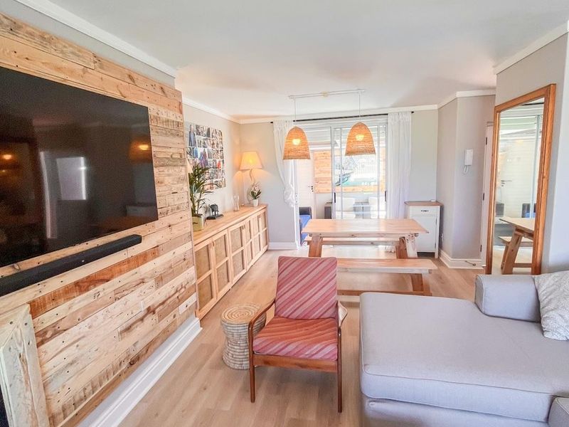Open plan living and dining area featuring a timber feature wall, light laminate flooring, and direct access to an outdoor patio through sliding glass doors.