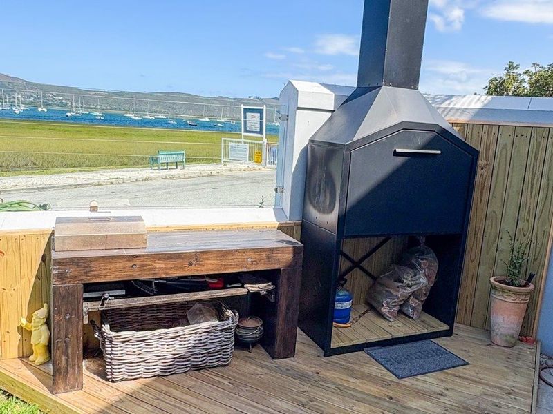 Outdoor patio area featuring timber decking, a built-in braai, and timber fencing, offering scenic views of the nearby estuary and boats.