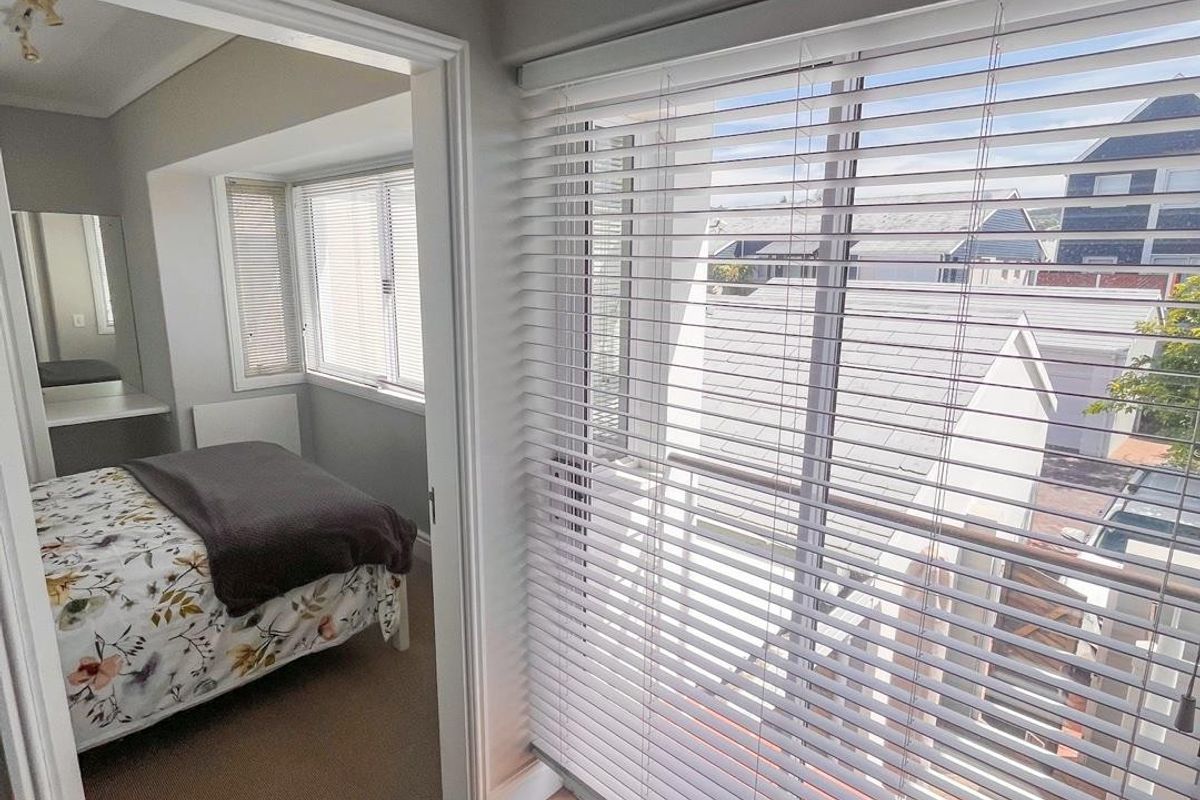 A bedroom featuring tiled and carpeted flooring, built-in vanity, and large windows with venetian blinds, offering a view of the surrounding neighborhood.