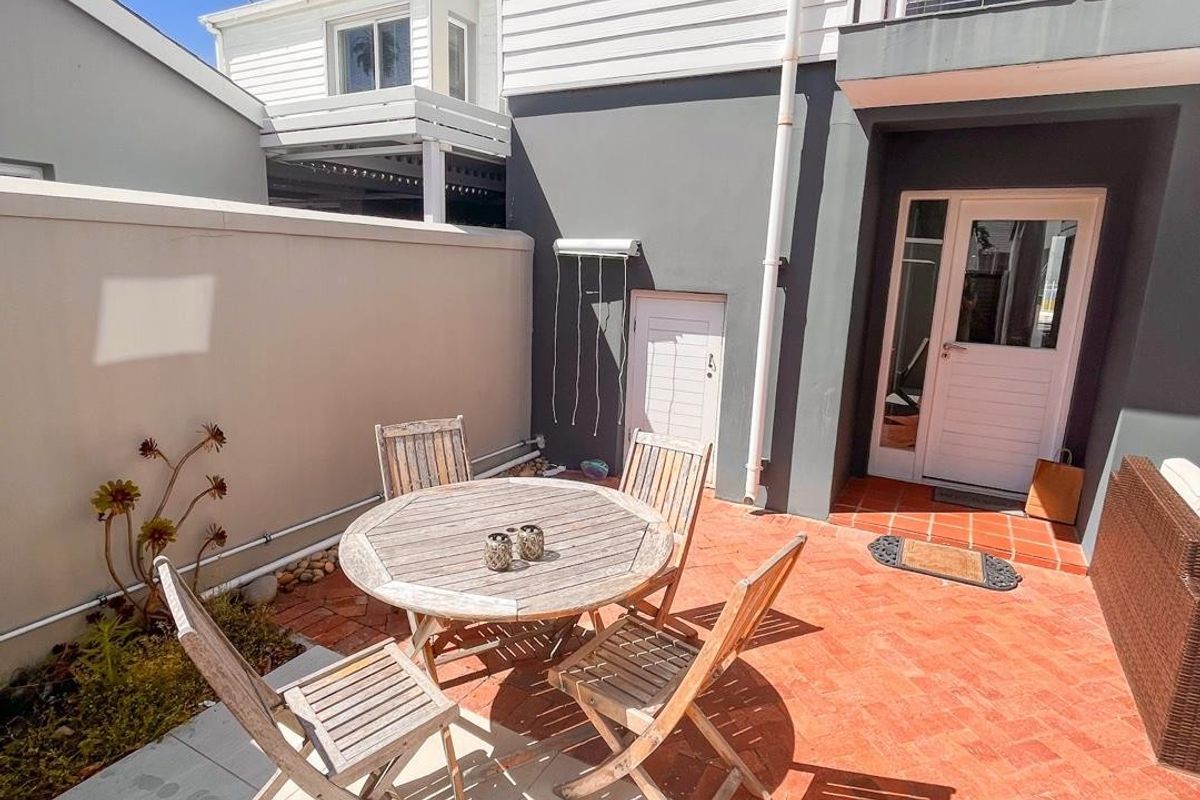A rear courtyard featuring a mix of brick and stone paving, providing direct access to the home through a glass-paneled door.