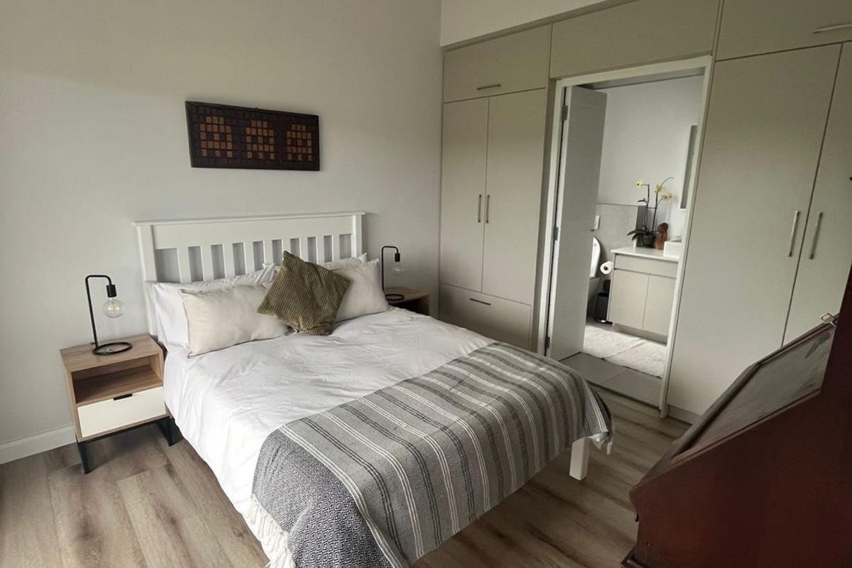 A well-maintained bedroom featuring light laminate flooring, extensive built-in wardrobe storage, and direct access to an en-suite bathroom.