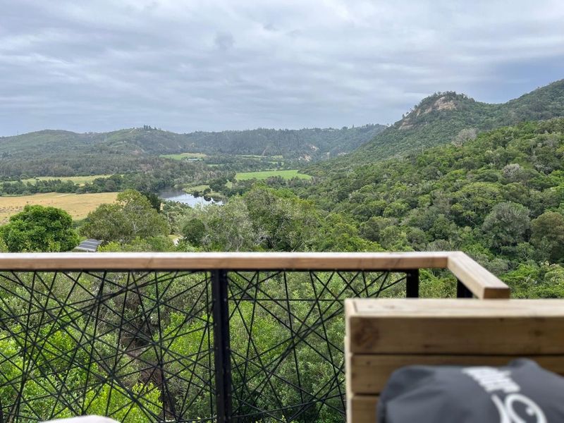 Scenic elevated view overlooking lush green hills, forest, and a river, framed by a modern metal and timber balustrade.