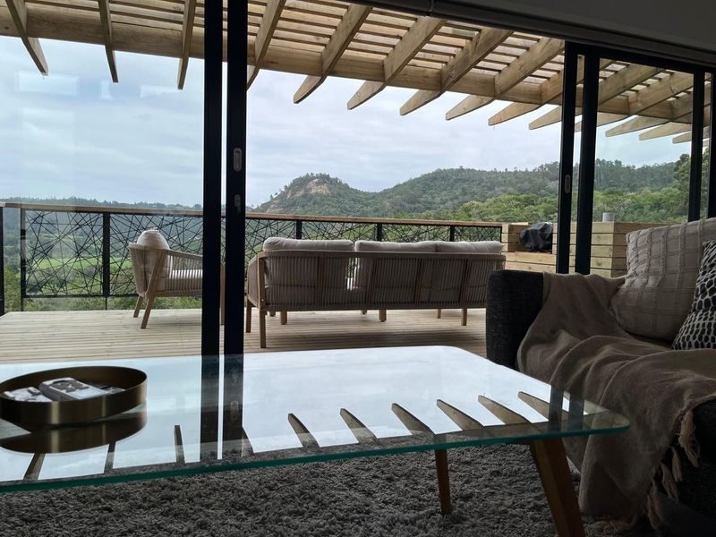 A spacious outdoor balcony featuring timber decking, a pergola structure, and decorative metal railings, offering scenic views of the surrounding hills.