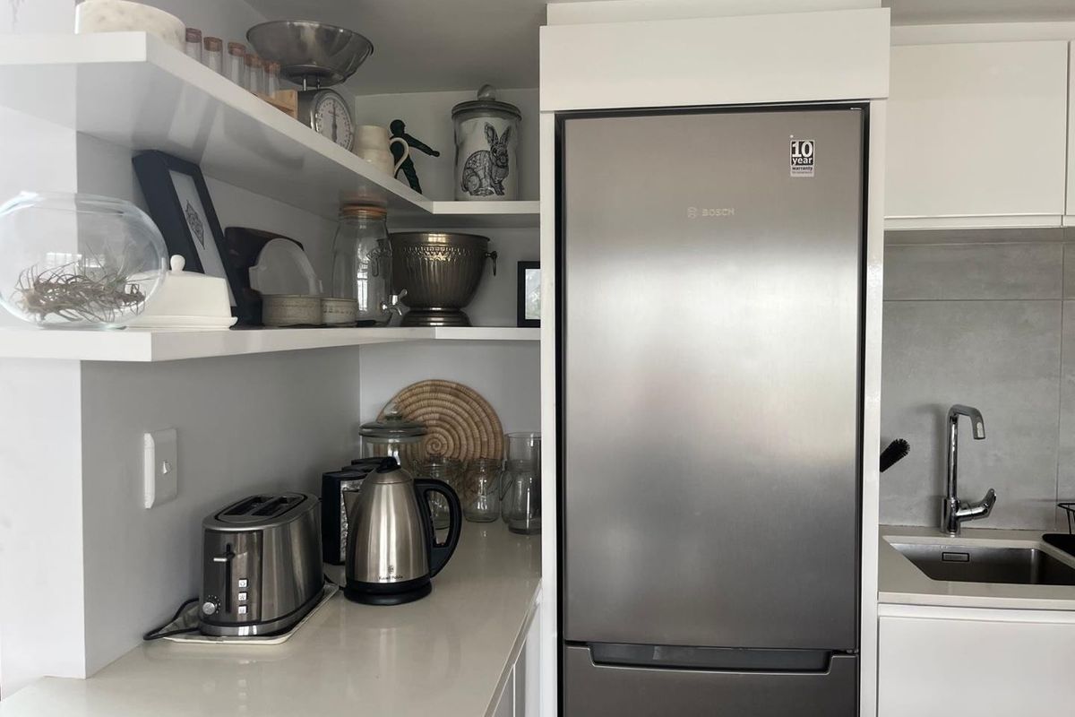 A modern kitchen area featuring clean white cabinetry, stone countertops, floating shelving, and a stainless steel sink with a contemporary mixer tap.