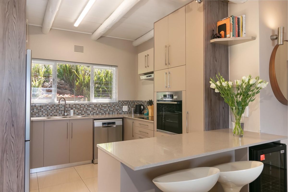 Modern kitchen featuring sleek built-in cabinetry, stone countertops, stainless steel appliances, a breakfast bar, and a bright window overlooking the garden.