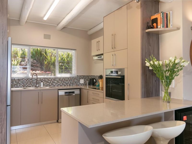 Modern kitchen featuring sleek built-in cabinetry, stone countertops, stainless steel appliances, a breakfast bar, and a bright window overlooking the garden.