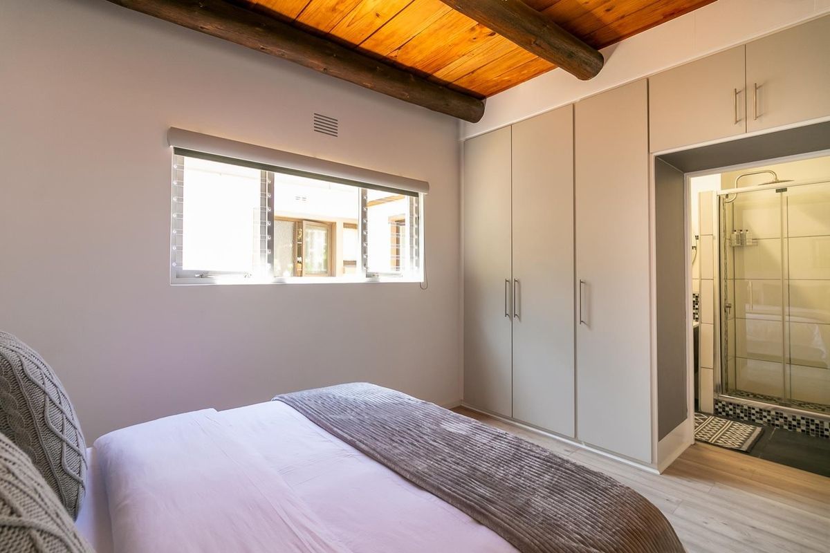 A well-maintained bedroom featuring built-in cupboards, exposed timber ceiling beams, and direct access to an en-suite bathroom with a shower.