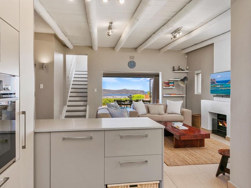 Open-plan living area featuring a modern kitchen with stone countertops, exposed beam ceilings, a cozy fireplace, and direct access to a scenic outdoor patio.
