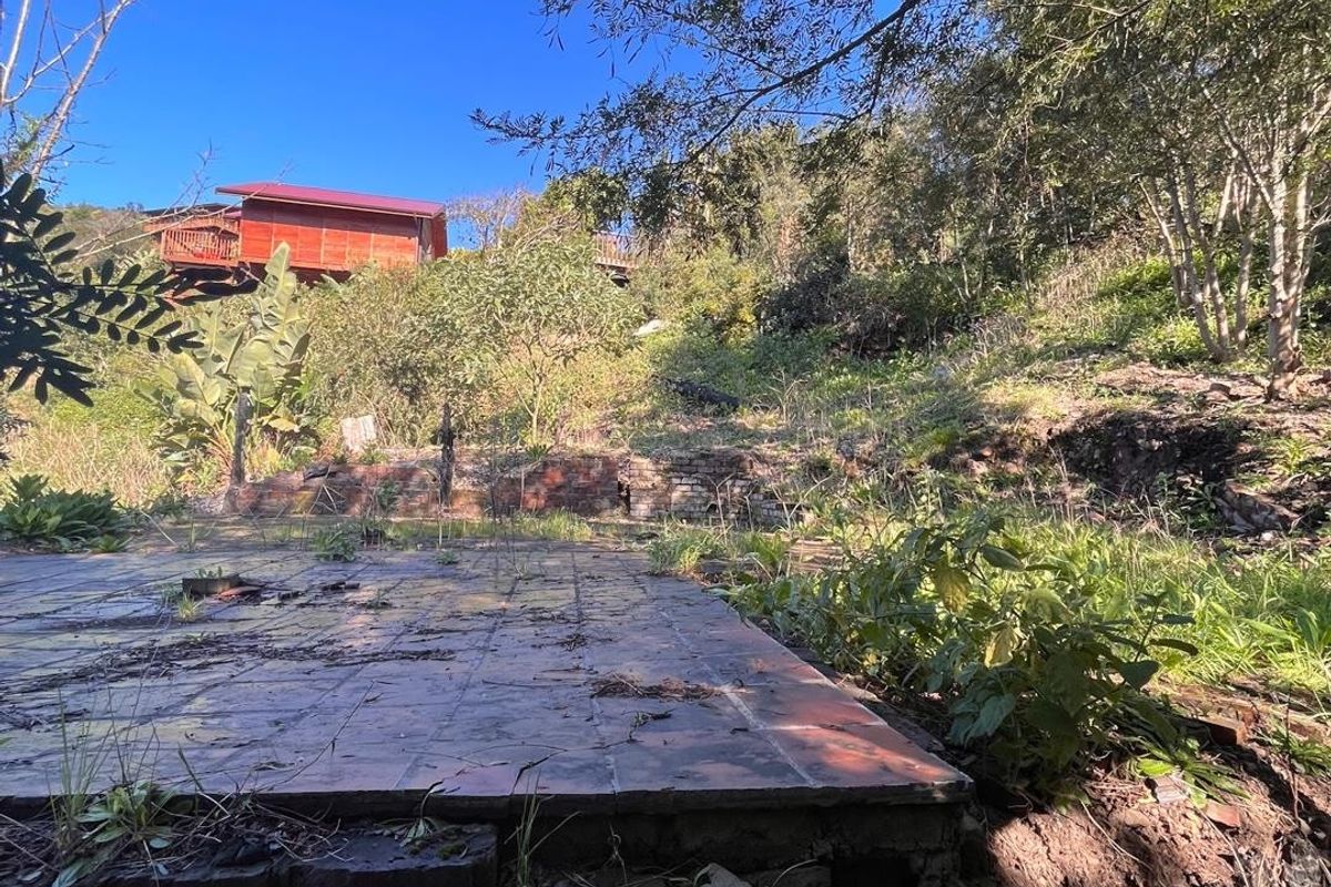 A sloped residential plot featuring a weathered brick retaining wall and a tiled patio base, surrounded by mature trees and natural vegetation.