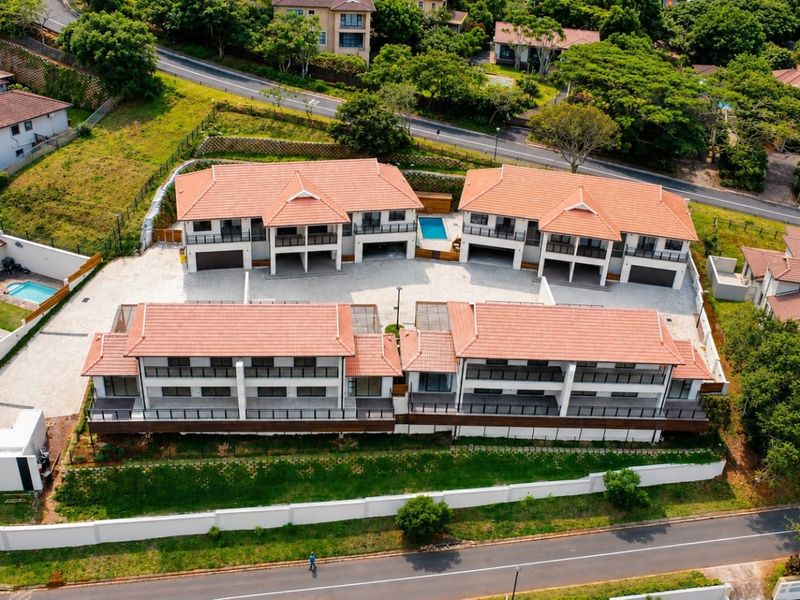 Aerial view of a modern townhouse complex featuring tiled roofs, paved driveways, private balconies, and a communal swimming pool within a landscaped estate.