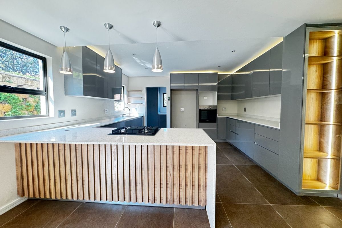 Modern kitchen featuring high-gloss cabinetry, stone countertops, a timber-accented island with a gas hob, built-in oven, and integrated display shelving.
