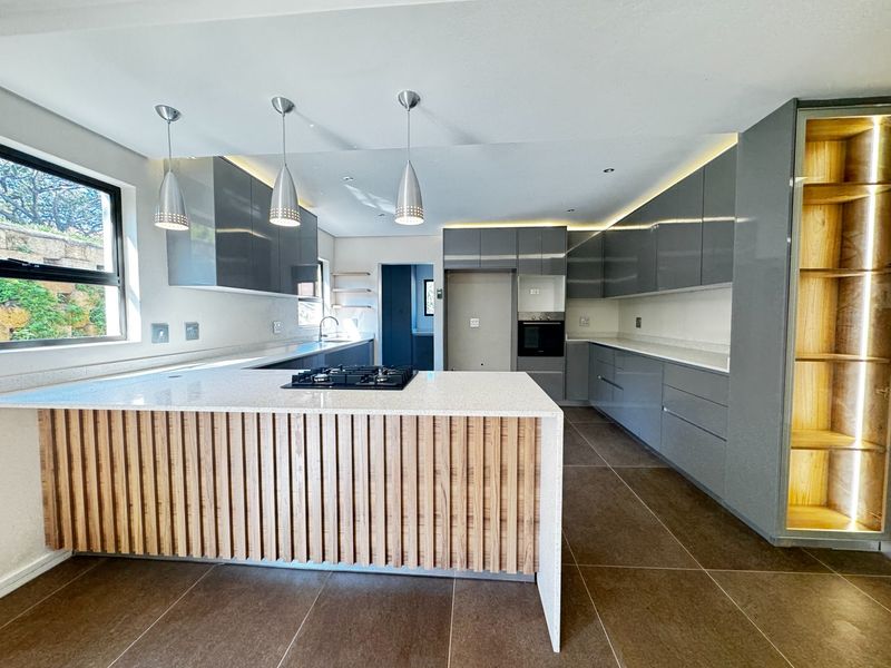 Modern kitchen featuring high-gloss cabinetry, stone countertops, a timber-accented island with a gas hob, built-in oven, and integrated display shelving.