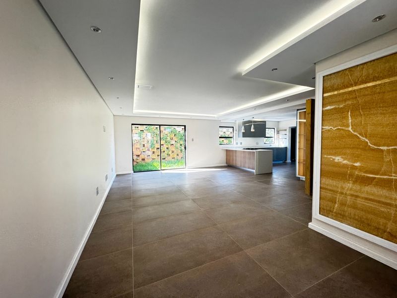 Spacious open-plan living and kitchen area featuring modern recessed lighting, large format floor tiles, and a striking stone feature wall.