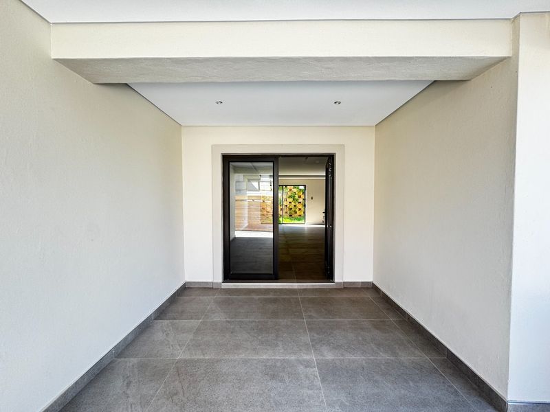 A clean, covered patio area featuring modern large-format floor tiles, recessed ceiling lighting, and a sliding glass door leading into the main living space.
