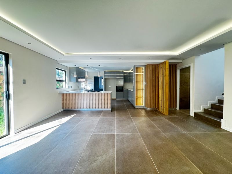 Modern open-plan living and kitchen area featuring sleek cabinetry, timber slat accents, recessed lighting, and large format floor tiles.