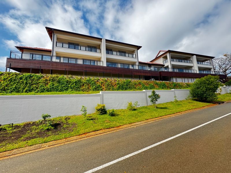 A view of the townhouse complex exterior featuring multi-level balconies with glass balustrades, a retaining wall, and landscaped garden beds.
