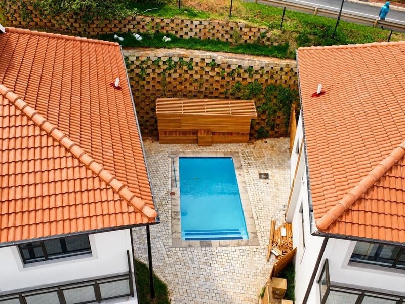 Aerial view of a townhouse courtyard featuring a swimming pool, timber pergola, and paved area between two structures with terracotta tiled roofs.