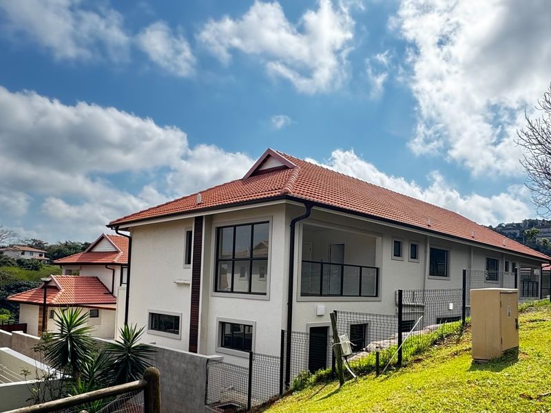 Rear view of a modern townhouse featuring terracotta roof tiles, a private balcony with glass balustrades, and black aluminium window frames.