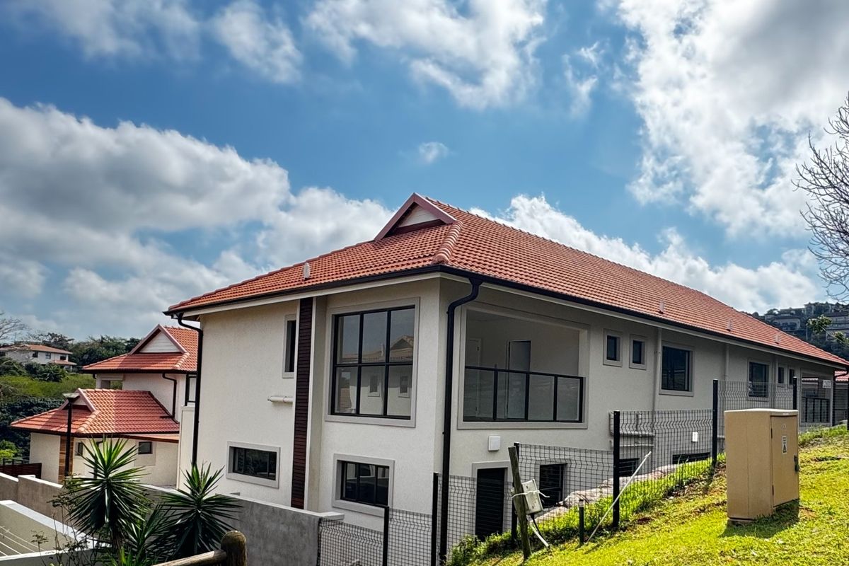 Rear view of a modern townhouse featuring terracotta roof tiles, a private balcony with glass balustrades, and black aluminium window frames.