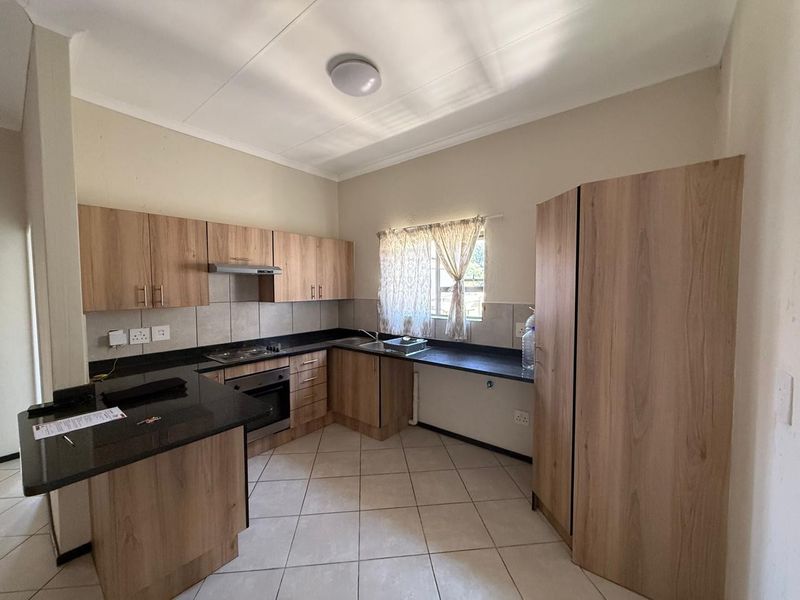 A clean, functional kitchen featuring wood-look laminate cabinetry, dark granite countertops, built-in oven, hob, and extractor fan with neutral tiled flooring.