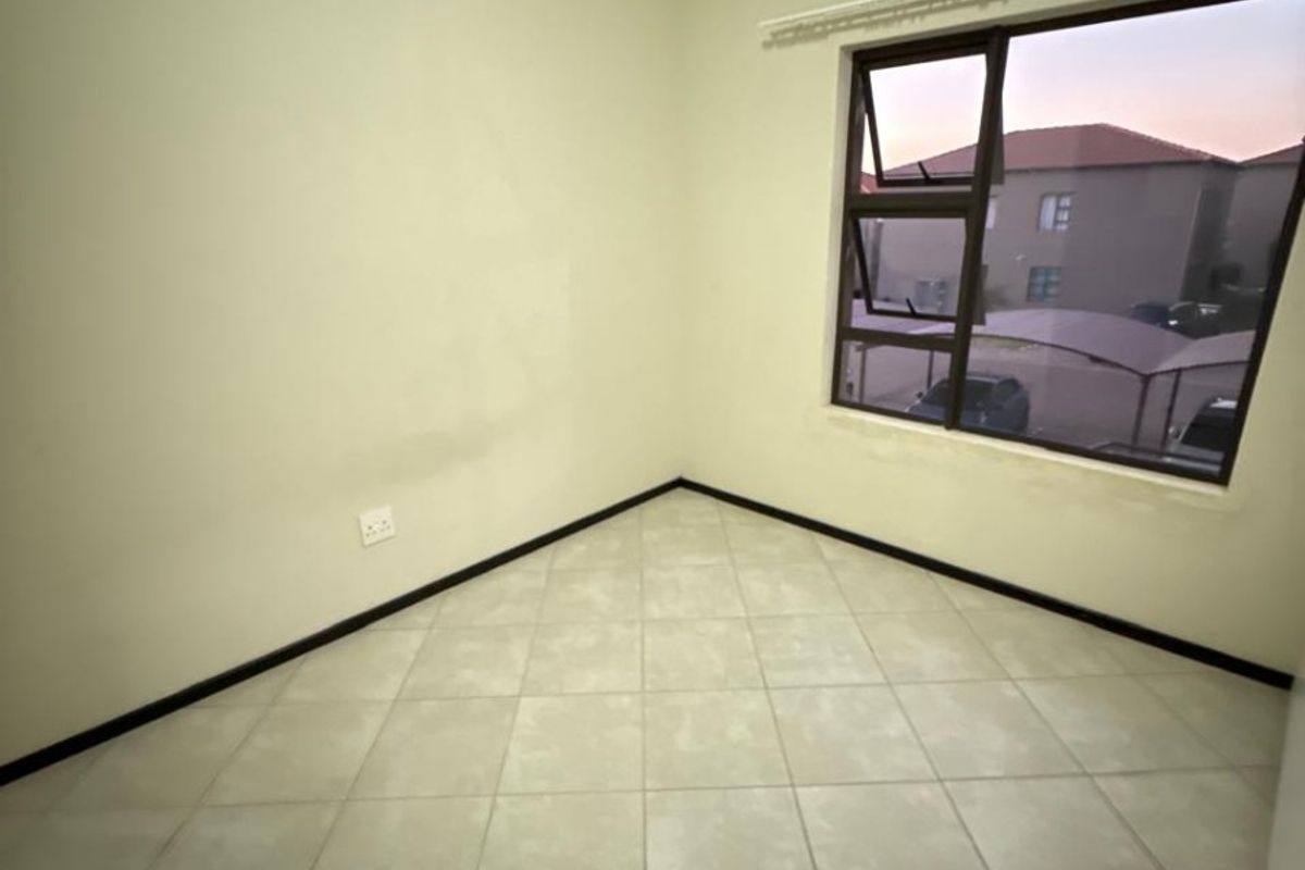 An empty bedroom featuring neutral tiled flooring, clean walls, and a large aluminium-framed window providing natural light.