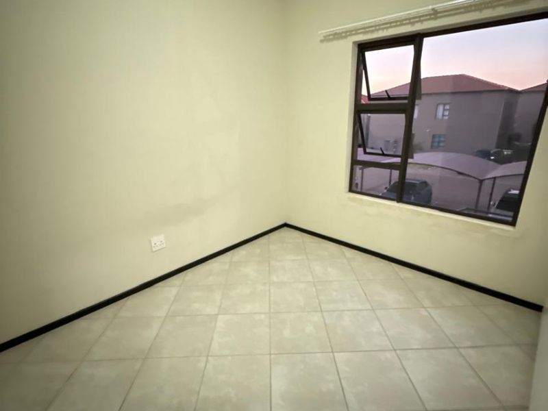 An empty bedroom featuring neutral tiled flooring, clean walls, and a large aluminium-framed window providing natural light.