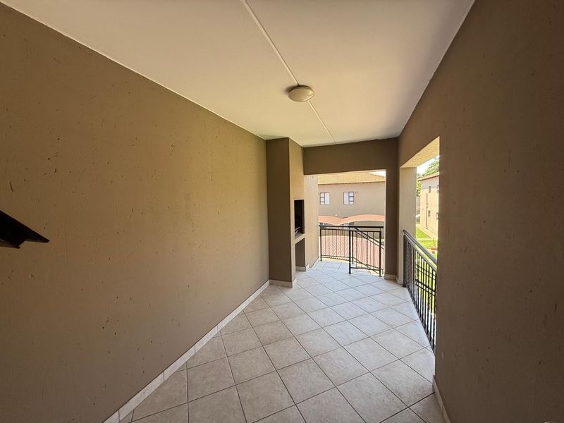 A covered balcony featuring tiled flooring, a built-in braai, and metal balustrades, offering an outdoor space suitable for relaxation.