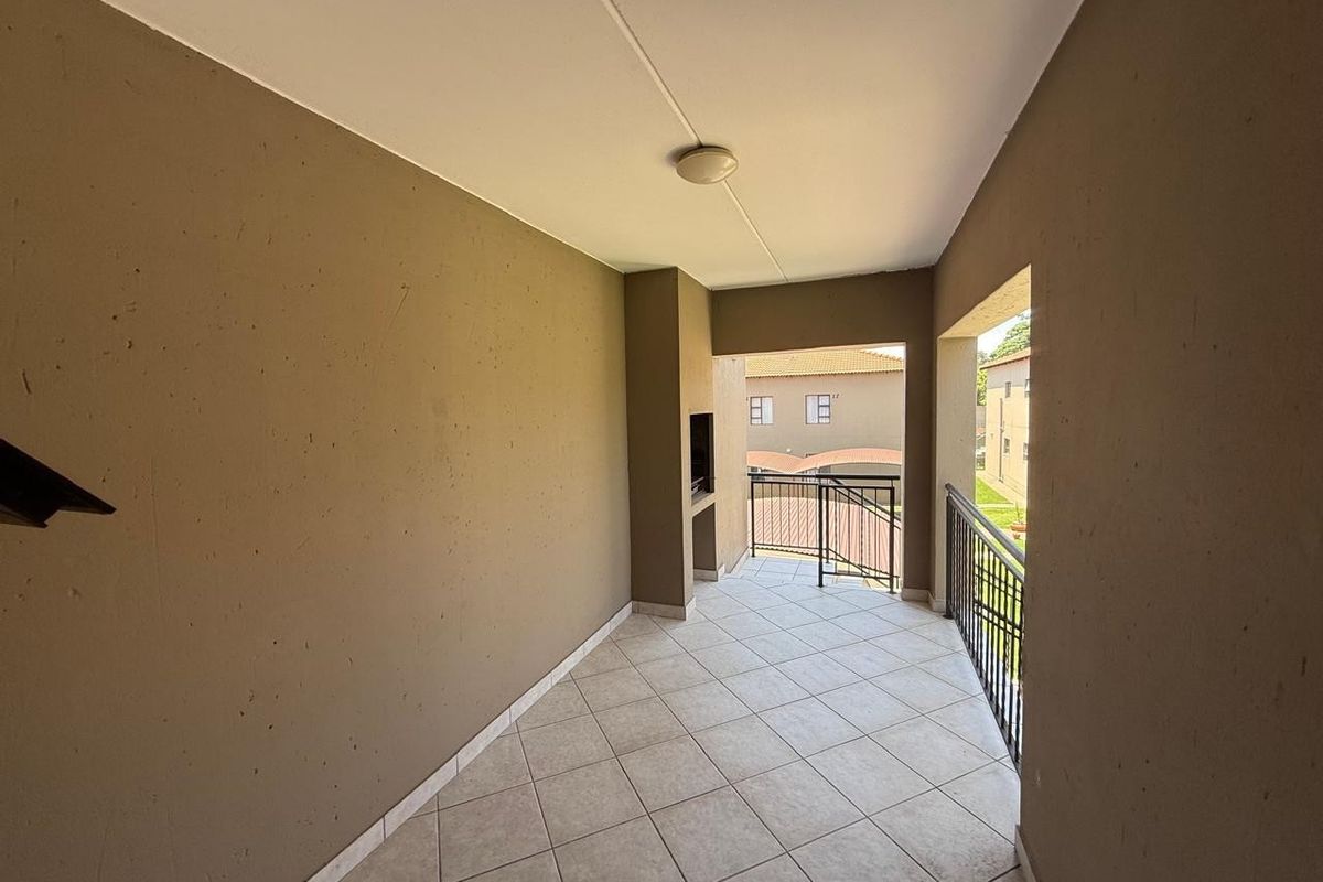 A covered balcony featuring tiled flooring, a built-in braai, and metal balustrades, offering an outdoor space suitable for relaxation.