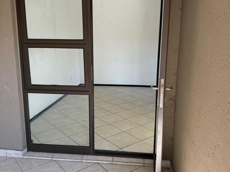 An exterior view of an entrance featuring a brown aluminium sliding door and neutral ceramic floor tiles leading into an empty interior space.
