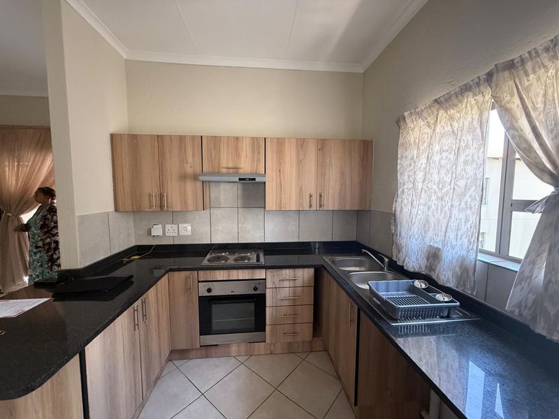 A functional kitchen featuring wood-finish cabinetry, granite countertops, a built-in oven, electric hob, and a double sink with tiled backsplash.