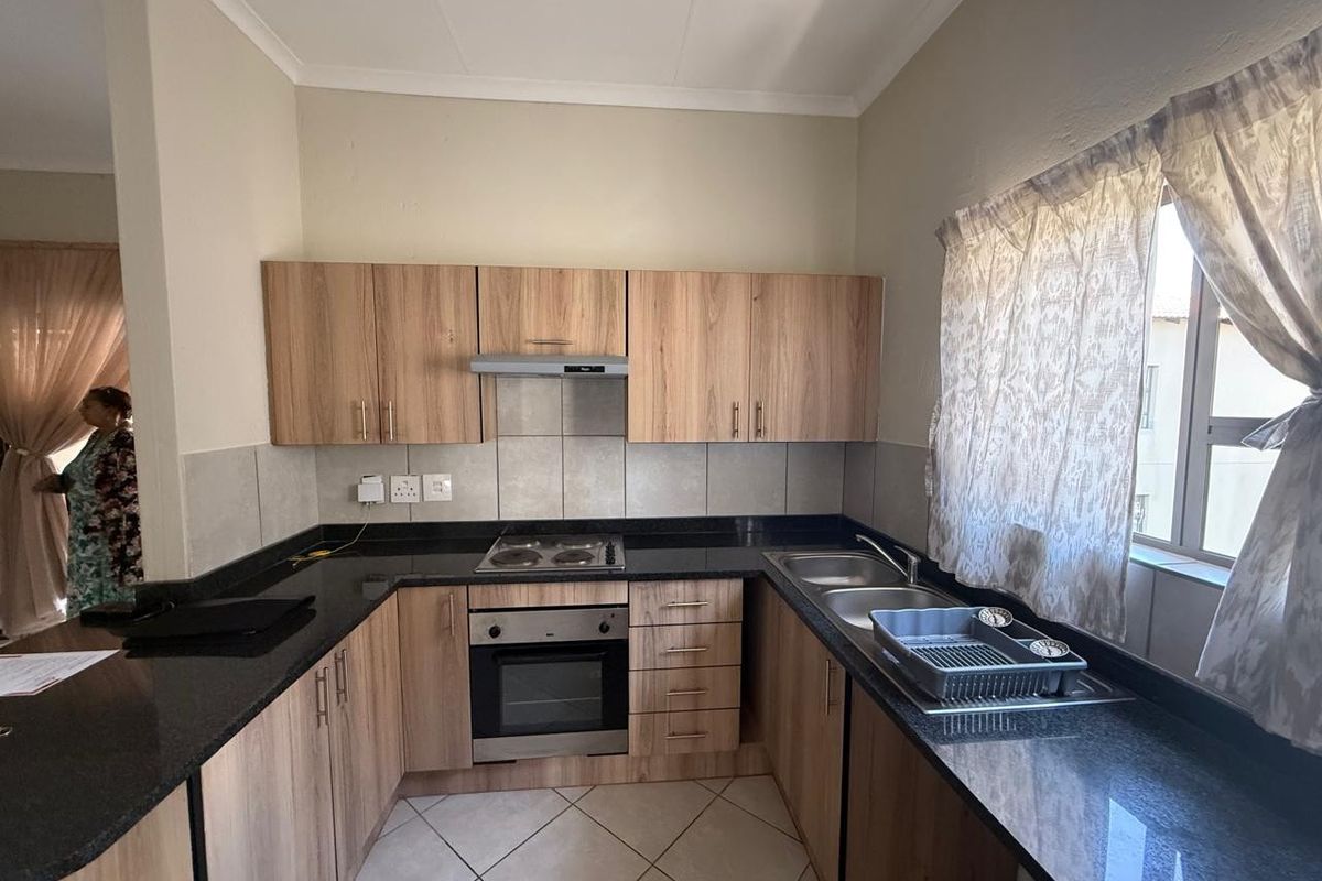A functional kitchen featuring wood-finish cabinetry, granite countertops, a built-in oven, electric hob, and a double sink with tiled backsplash.