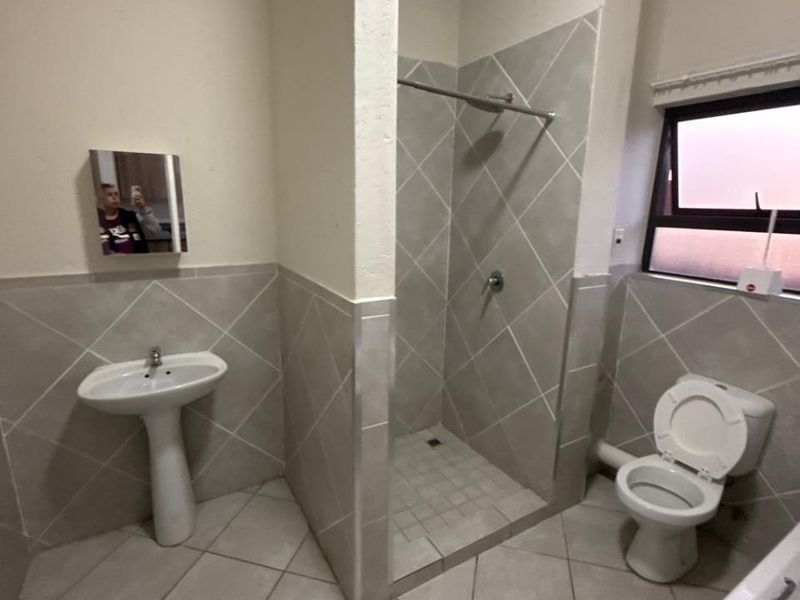 A functional bathroom featuring a pedestal basin, shower enclosure, toilet, and bathtub with neutral tiled finishes throughout.