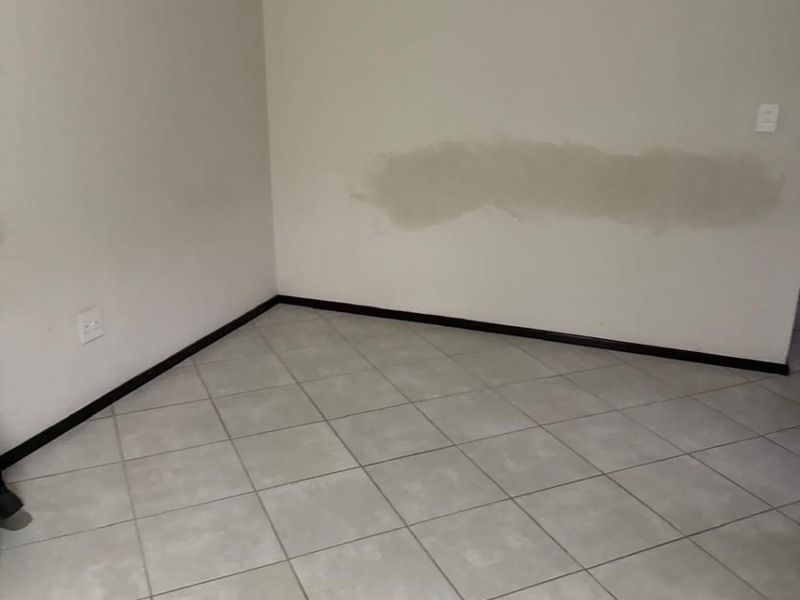 An empty bedroom featuring ceramic floor tiles and visible wall patch repairs, requiring cosmetic attention to restore the finish.