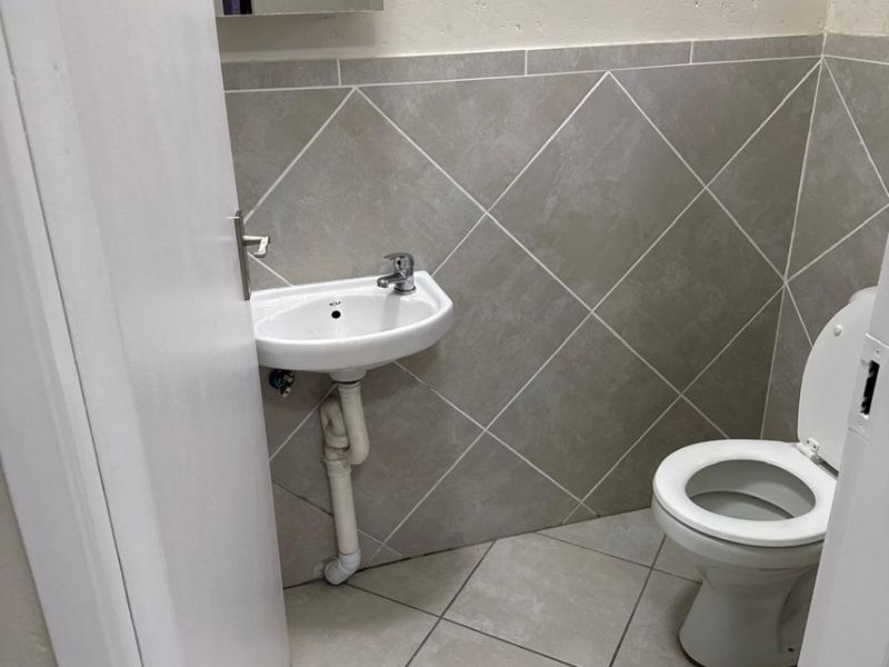 A compact guest bathroom featuring tiled walls and flooring, a wall-mounted basin, and a standard toilet.