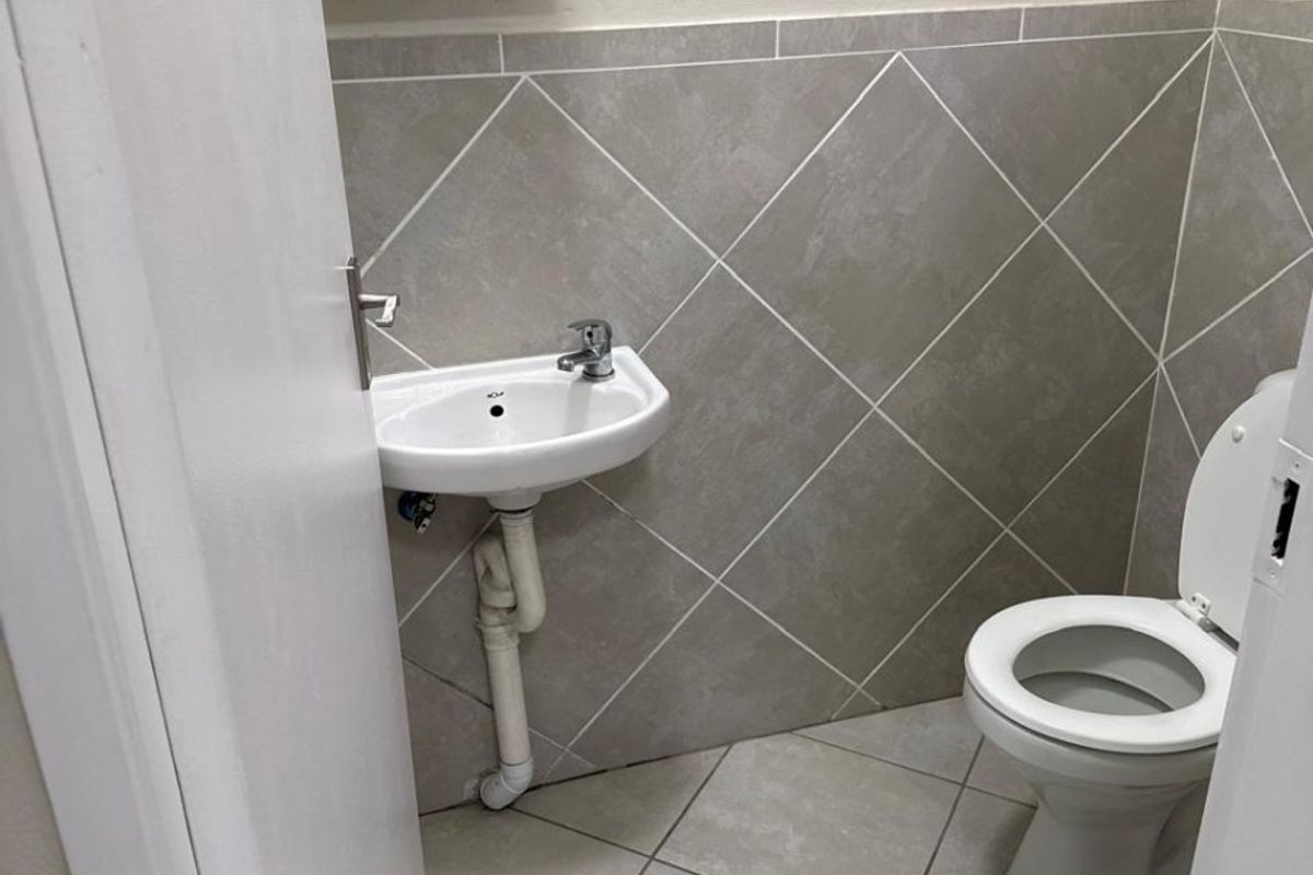 A compact guest bathroom featuring tiled walls and flooring, a wall-mounted basin, and a standard toilet.