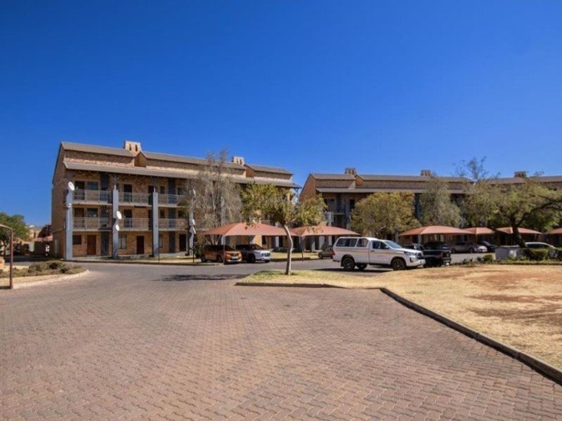 Exterior view of a multi-story apartment complex featuring paved driveways and covered parking bays within a residential estate setting.