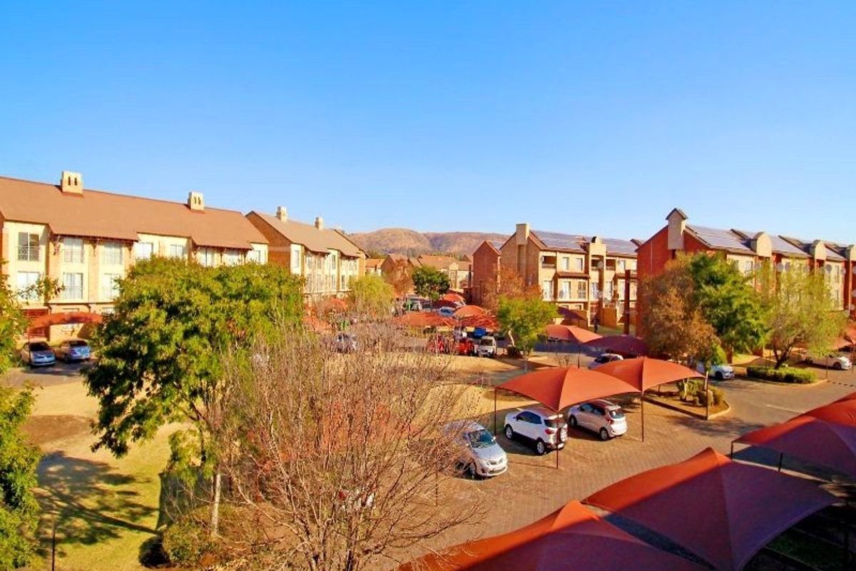 Aerial view of an apartment complex featuring multiple residential buildings, paved parking areas with shade cloth carports, and landscaped grounds.