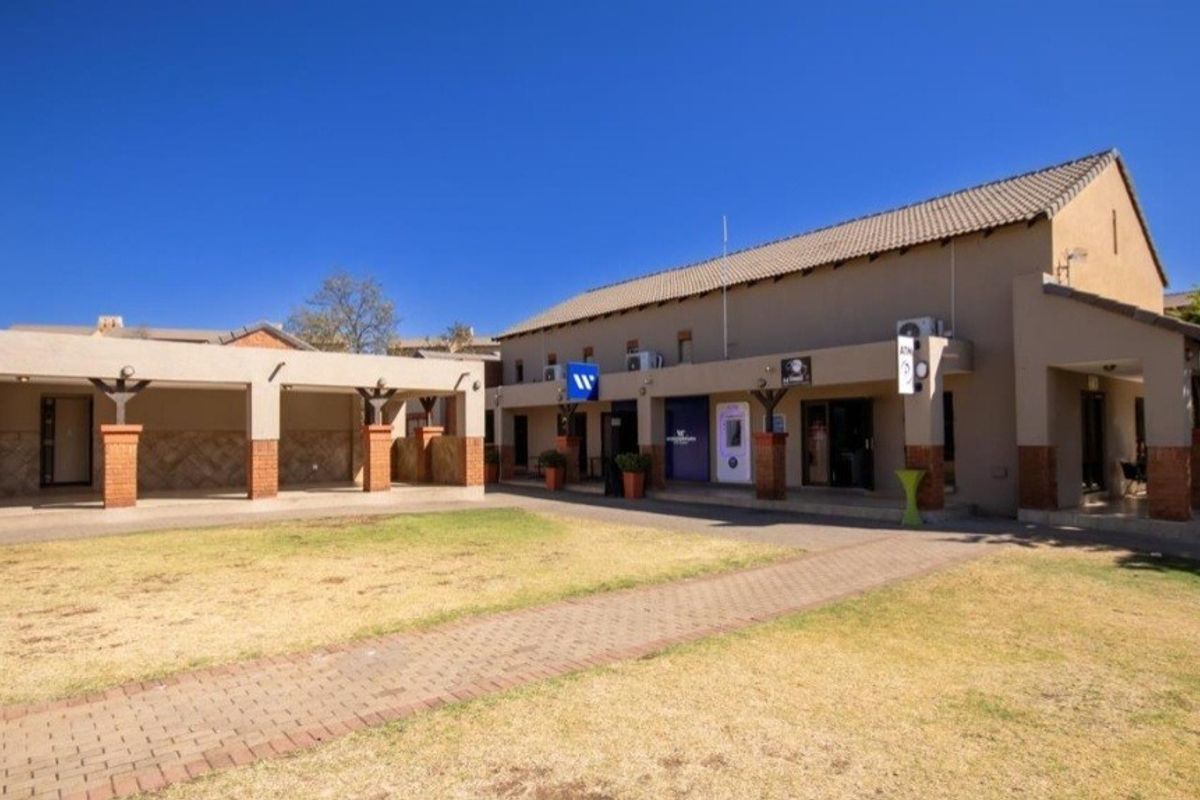 Exterior view of a commercial or apartment complex courtyard featuring a paved walkway, covered patio areas, and a central lawn.