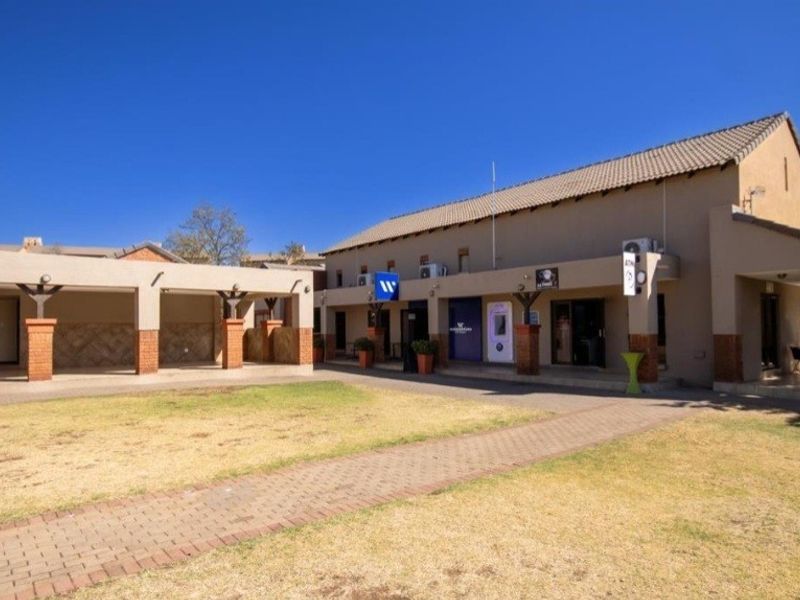 Exterior view of a commercial or apartment complex courtyard featuring a paved walkway, covered patio areas, and a central lawn.
