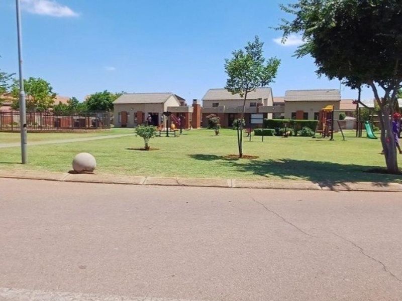 A well-maintained communal garden area within the apartment complex, featuring landscaped lawns, paved pathways, and established trees.