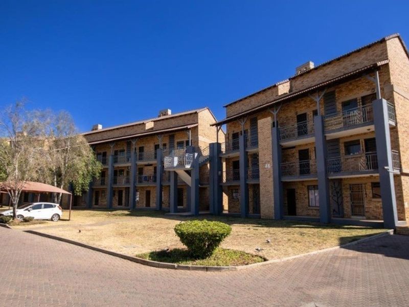 Exterior view of a multi-story face-brick apartment complex featuring covered parking bays, paved driveways, and private balconies.