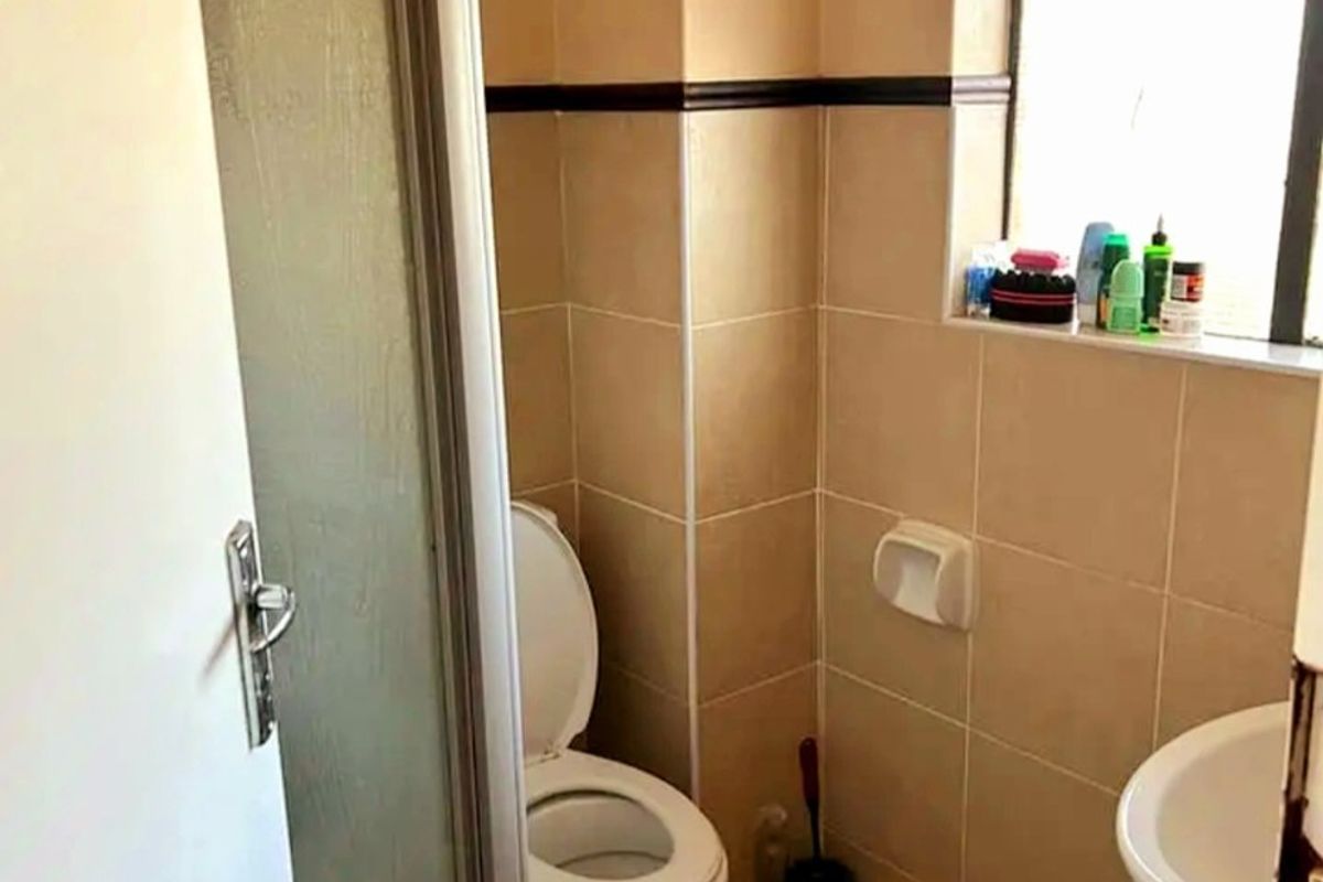 A functional bathroom featuring a pedestal basin, toilet, and a shower enclosure with tiled finishes and natural light from a window.