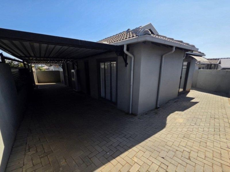 Rear exterior view featuring a covered carport, paved driveway, and access to the home via sliding doors.