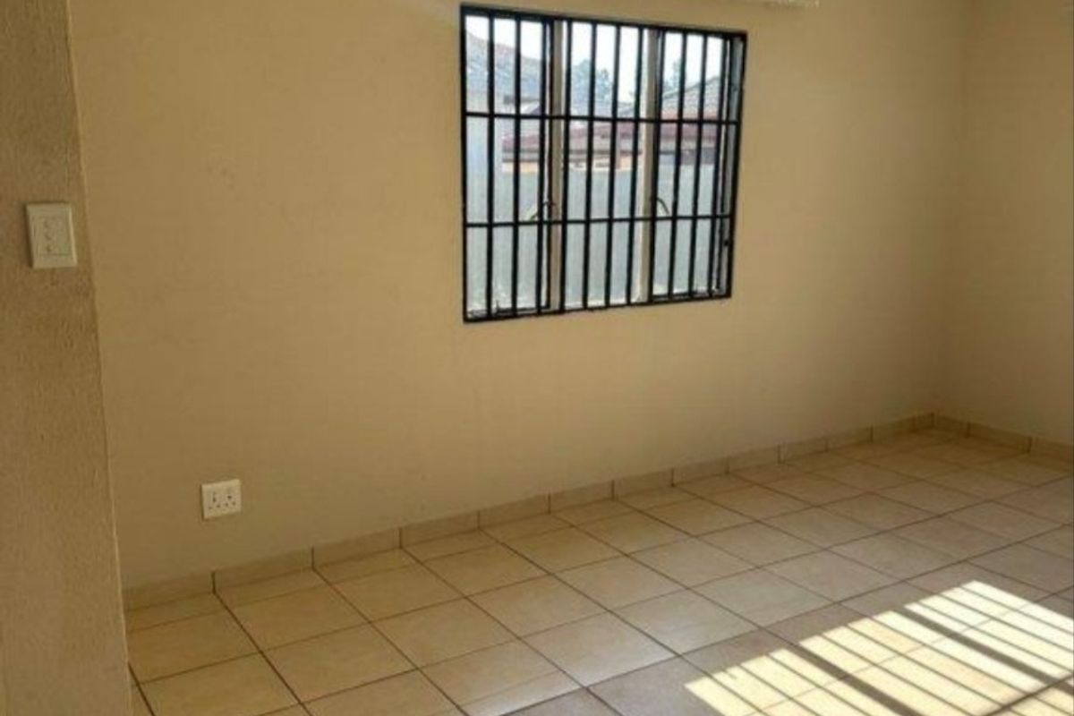 A clean, empty bedroom featuring neutral wall paint, tiled flooring, and a window fitted with security bars.