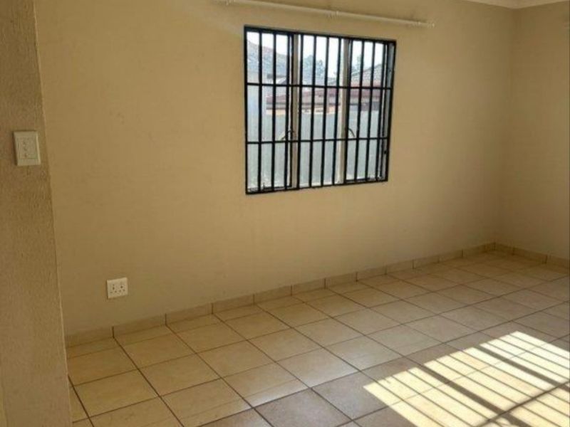 A clean, empty bedroom featuring neutral wall paint, tiled flooring, and a window fitted with security bars.
