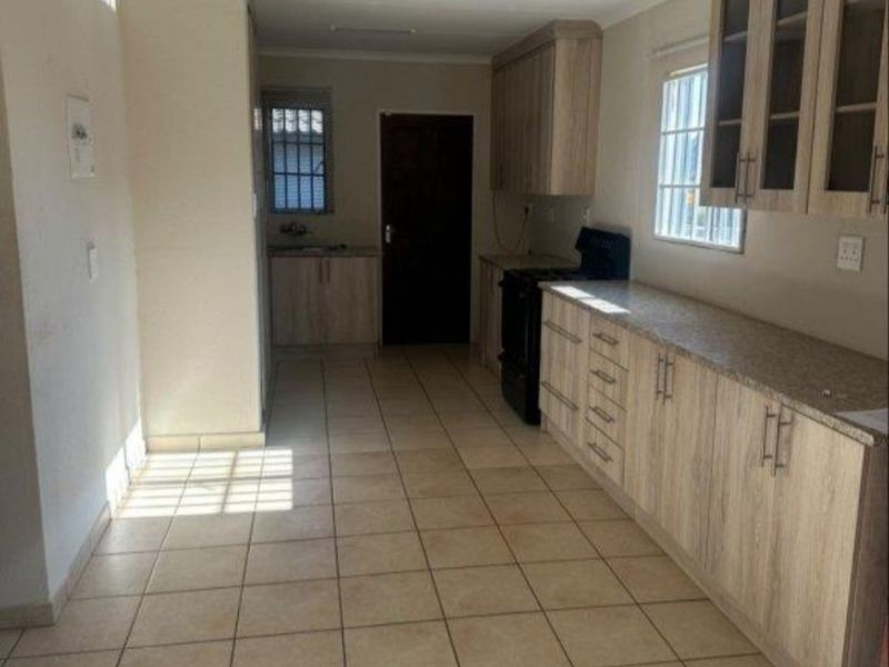 A functional kitchen featuring light wood-finish cabinetry, laminate countertops, tiled flooring, and a freestanding stove, with security bars installed on the windows.