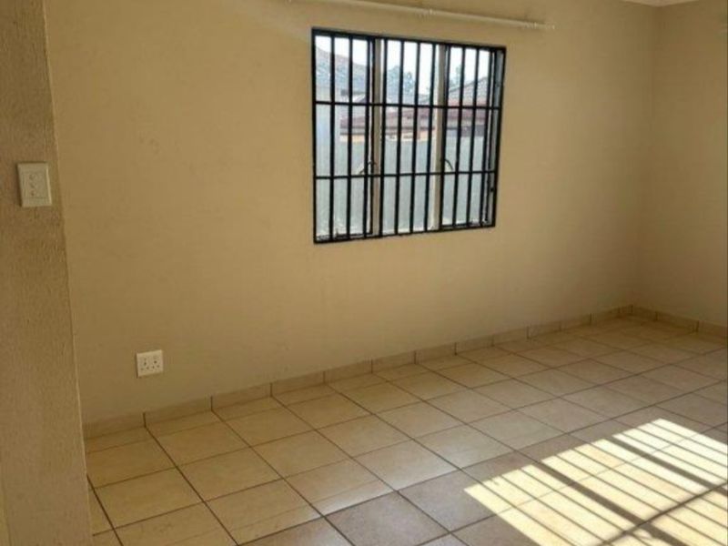 An empty living room featuring neutral tiled flooring, a window with security bars, and a curtain rail, offering a clean and versatile space.