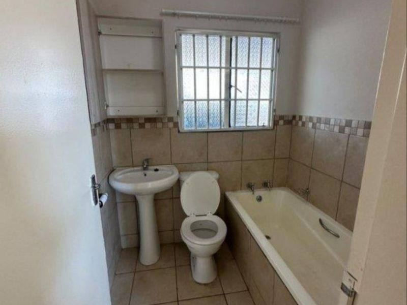 A functional bathroom featuring a pedestal basin, toilet, and bathtub with tiled finishes and security bars on the window.