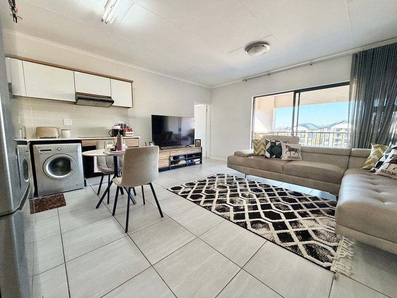 Open-plan living area featuring a modern kitchen with built-in cabinetry, tiled flooring, and a sliding door leading to a private balcony.