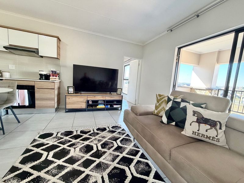 Modern open-plan living area featuring tiled floors, a compact kitchen with built-in cabinetry, and a sliding door leading to a balcony.
